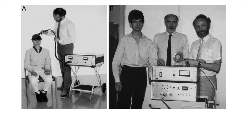 (A) Anthony T. Barker při demonstraci transkraniální magnetické stimulace (TMS) v Londýně, 1985. (B) Anthony T. Barker (vpravo), Ian L. Freeston (uprostřed) a Reza Jalinous (vlevo) představují zařízení pro TMS v roce 1985.